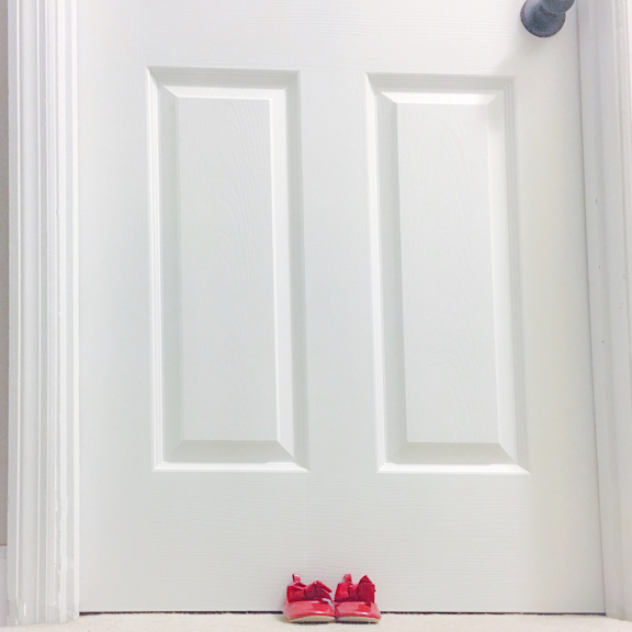 two red childrens shoes in front of a white door
