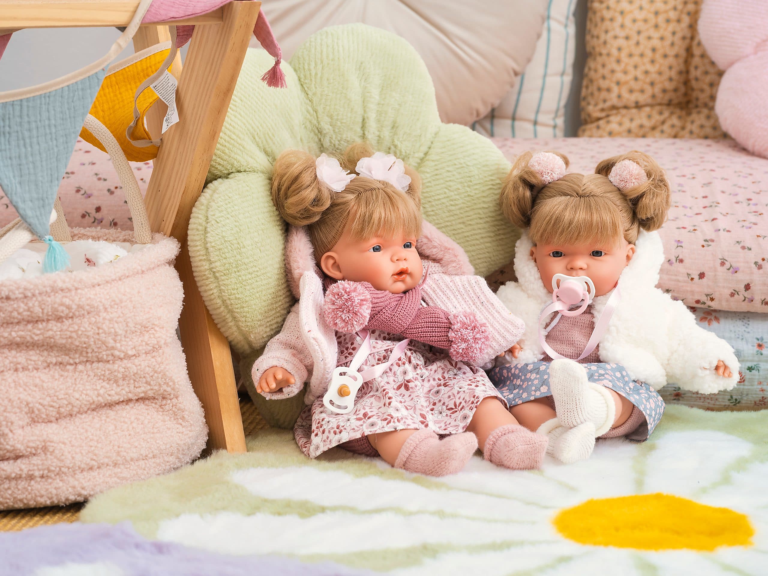 Two reborn dolls in knitted cardigans, seated together in a child's playroom