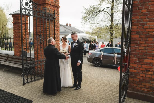 Ksiądz wita parę młodą przed bramą kościoła