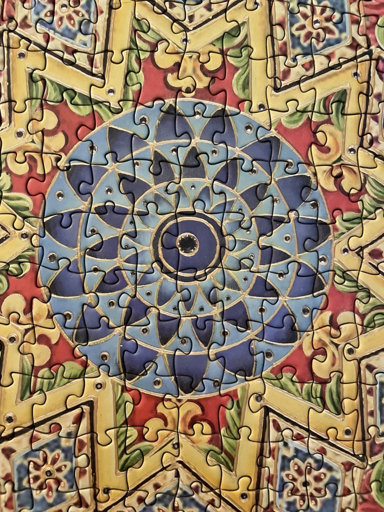 Close-up of a symmetrical, geometric mandala-style design featuring a blue central starburst on a yellow and red background.
