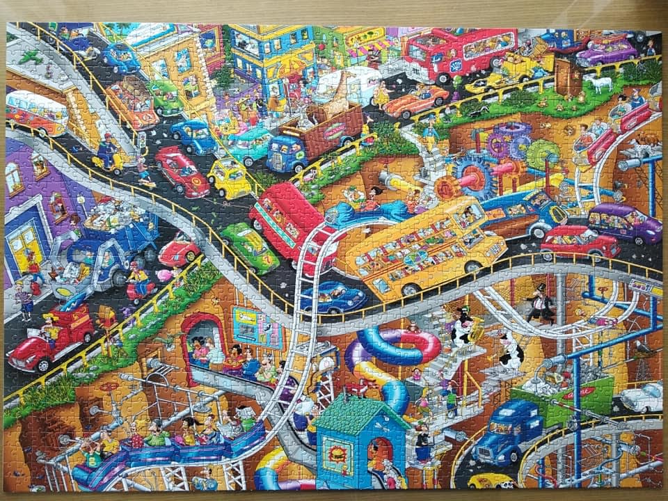 A chaotic, high-angle cartoon illustration of a multi-level city with winding roads, vehicles, and quirky characters.