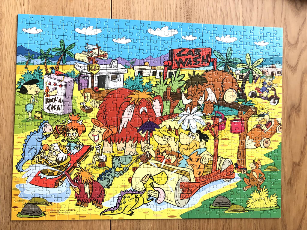 Cartoon scene featuring the Flintstones characters, dinosaurs, and a prehistoric town.