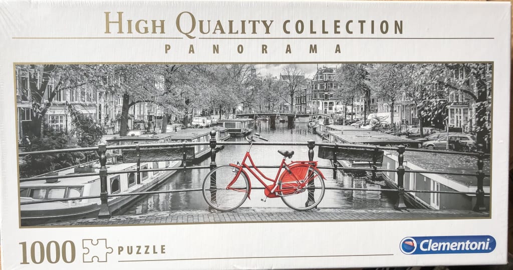 A vibrant red bicycle parked on a canal bridge in a black and white Amsterdam cityscape.