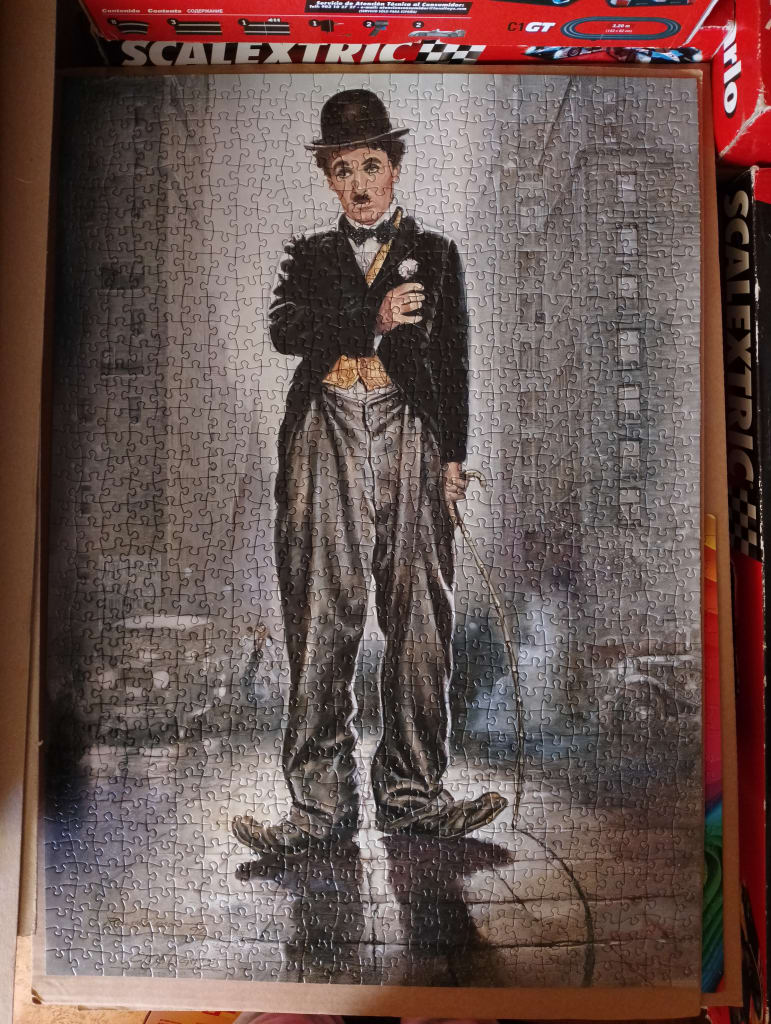 A portrait of Charlie Chaplin as The Tramp standing on a city street.