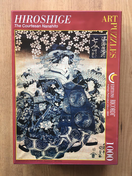 A traditional ukiyo-e style woodblock print featuring a standing courtesan dressed in an ornate, deep blue patterned kimono.