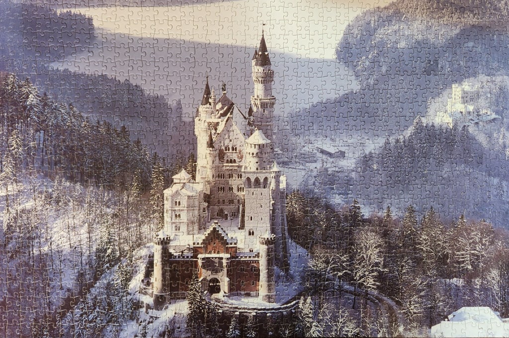 Aerial view of Neuschwanstein Castle in Bavaria surrounded by a snow-covered forest in winter.