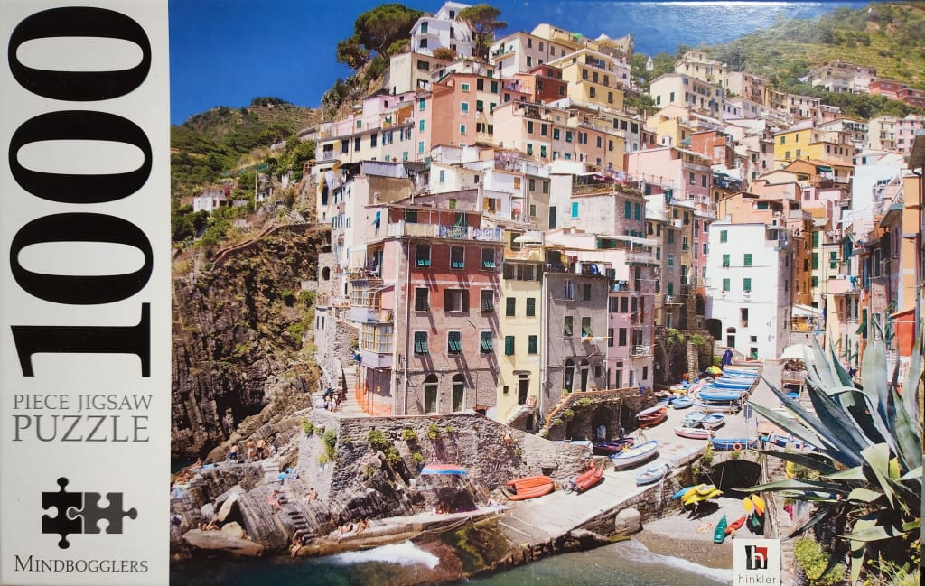A scenic photograph of the Italian seaside village of Riomaggiore, showing pastel buildings perched on a cliffside.