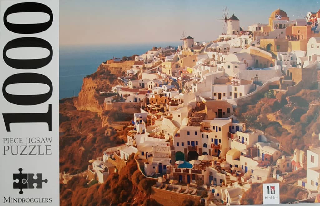 Coastal view of Oia, Santorini, with white buildings, blue domed roofs, and windmills perched on a cliff at sunset.