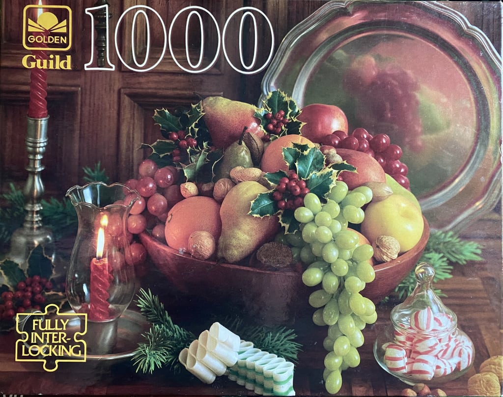 A still life arrangement of winter fruits, nuts, grapes, and candy in a wooden bowl with candles and holiday greenery.