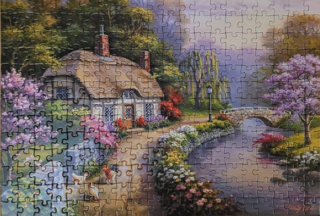 A charming thatched-roof cottage nestled by a stream with blooming lilac trees and a stone bridge.