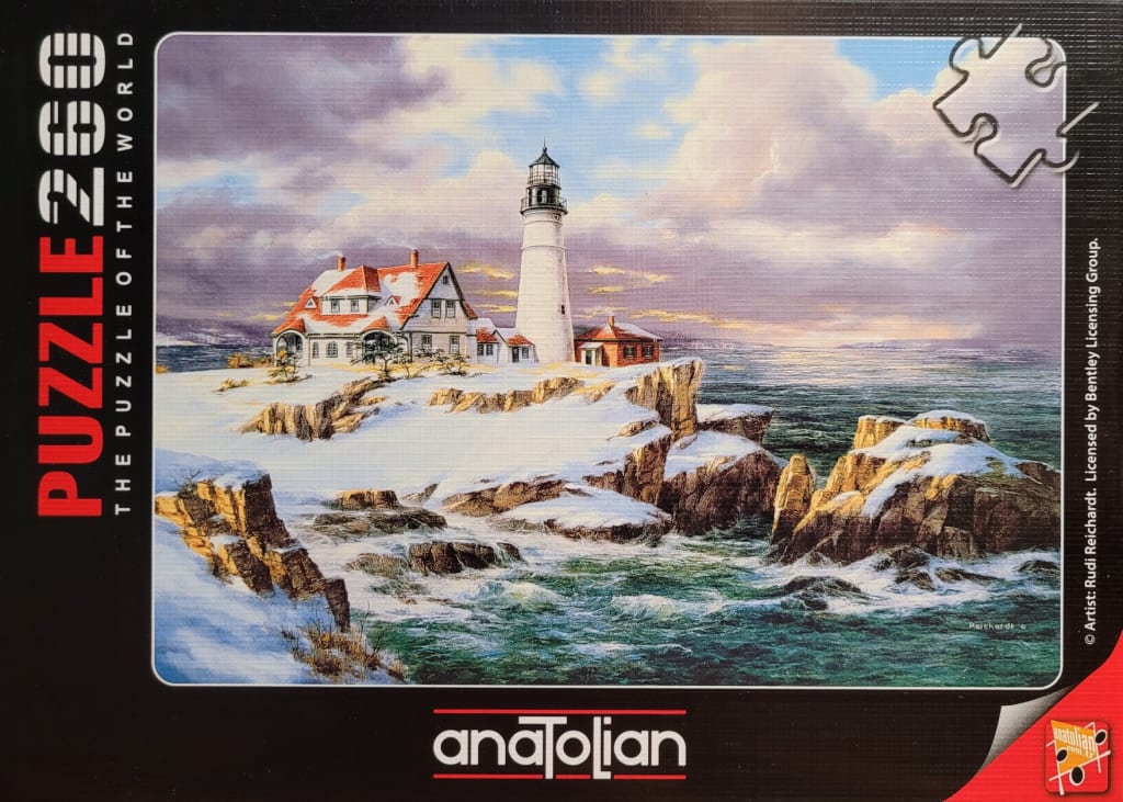 A lighthouse and keeper's cottage on a snowy, rocky cliff overlooking the ocean at sunset.
