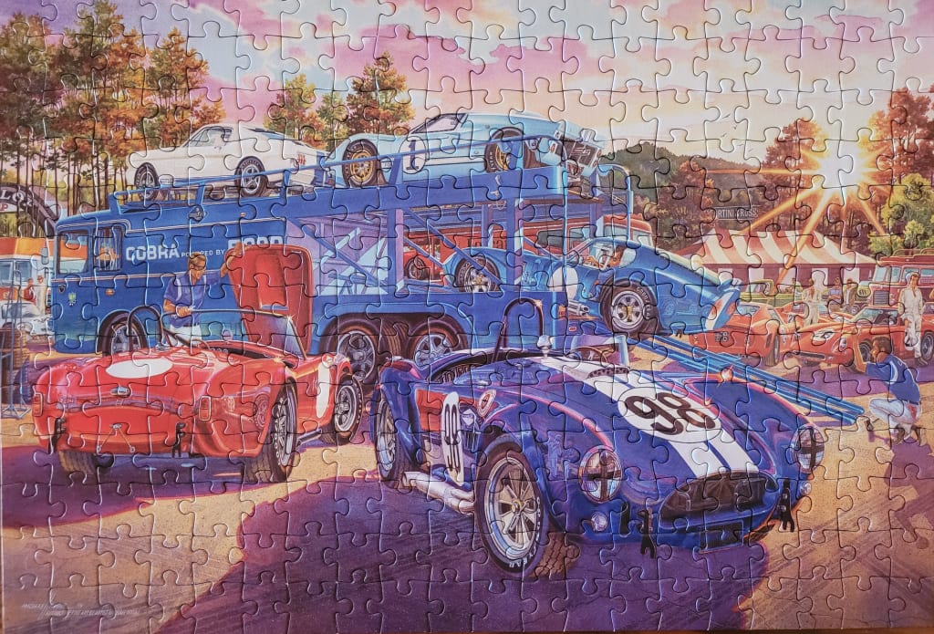 A vintage racing scene featuring Shelby Cobra cars at a track side during a sunset.