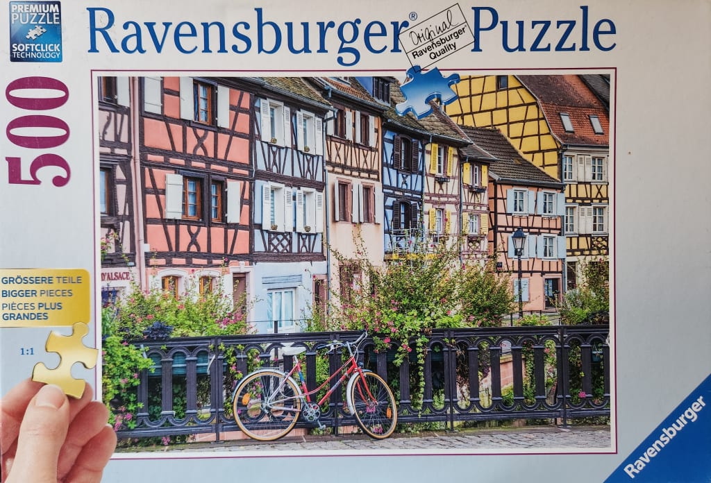 A red bicycle parked along a fence in front of colorful half-timbered houses in Alsace, France.