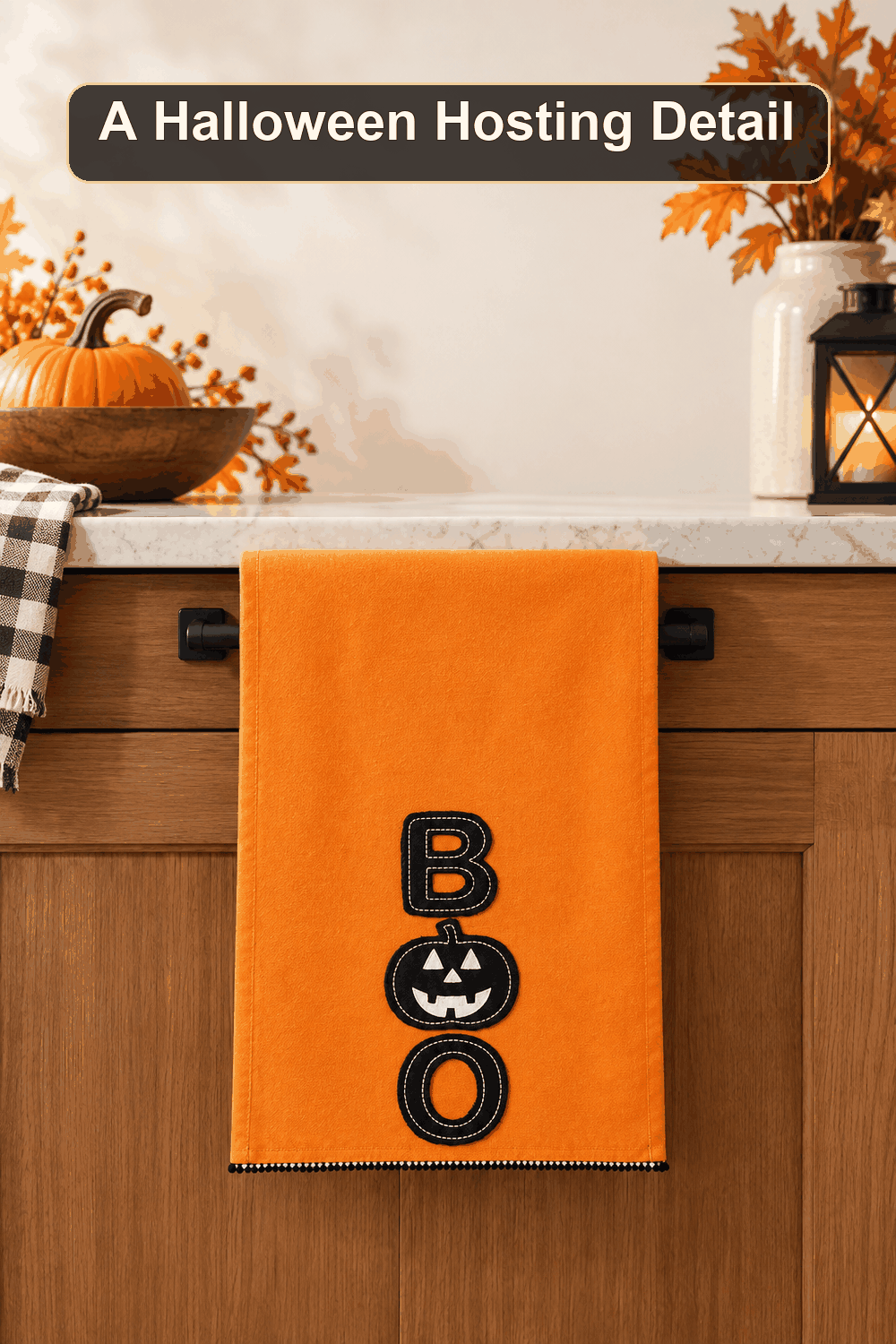 Styled Halloween home scene featuring the Orange Boo Kitchen Towel, 16x26, with the words A Halloween Hosting Detail in a dark banner above.