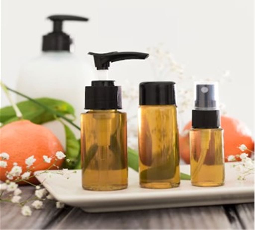 Amber pump and spray bottles beside oranges and small white flowers