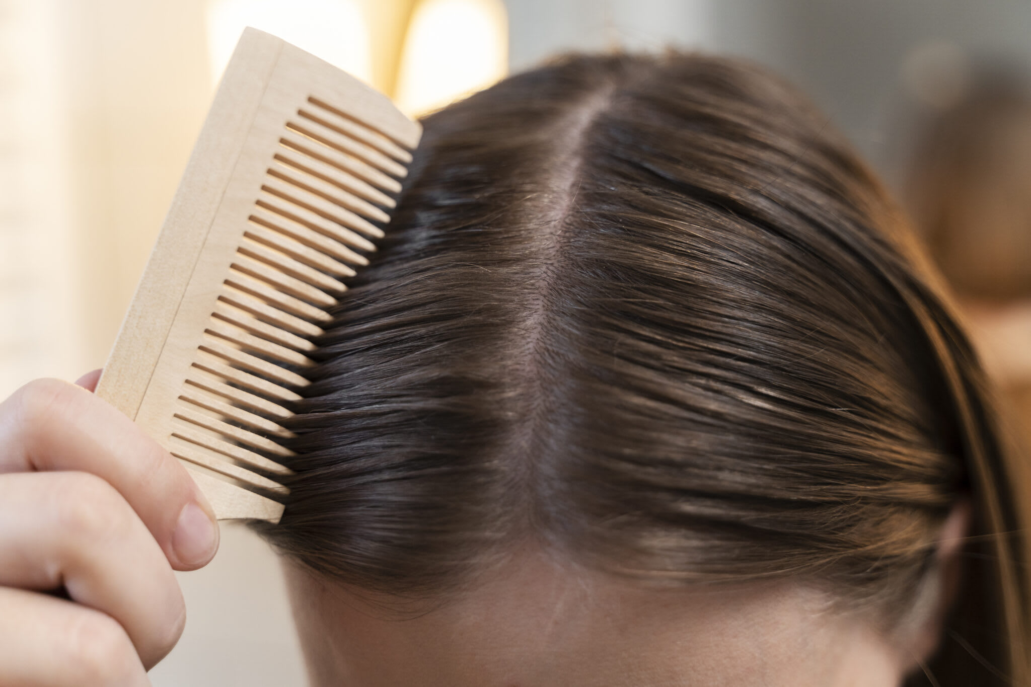 A wooden comb drawn through hair at the parting
