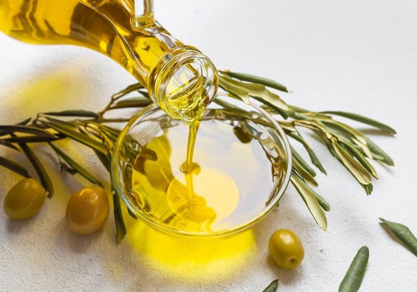 Golden oil poured into a glass bowl beside an olive branch