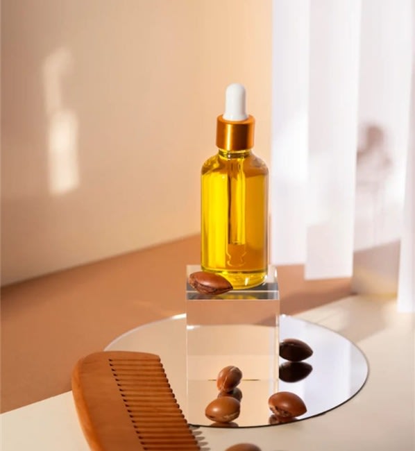 A dropper bottle of argan oil beside argan kernels and a wooden comb