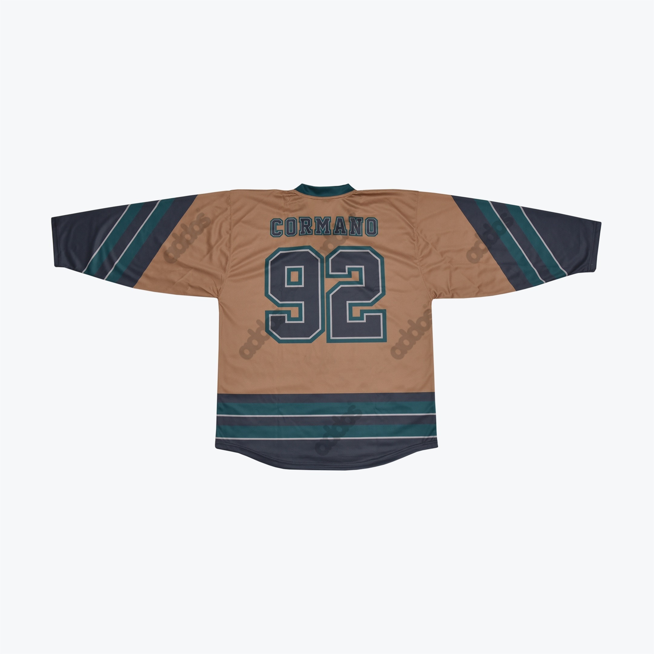 The back of a tan hockey jersey with CORMANO and 92 printed in dark teal and navy block letters, featuring striped sleeves and hem.