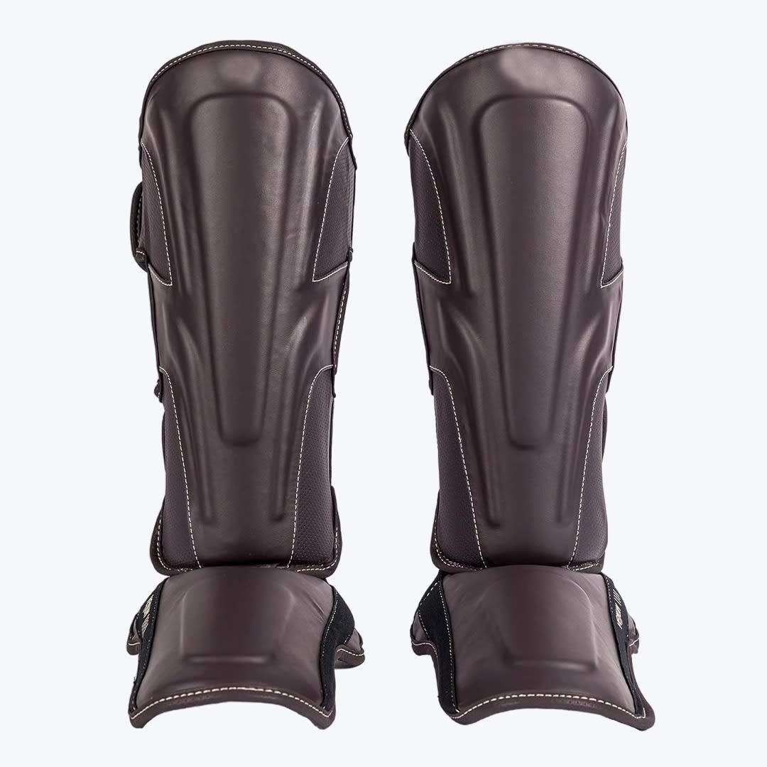 Brown Leather Shin Guards A pair of dark brown leather shin guards with instep protection, standing upright against a white background.