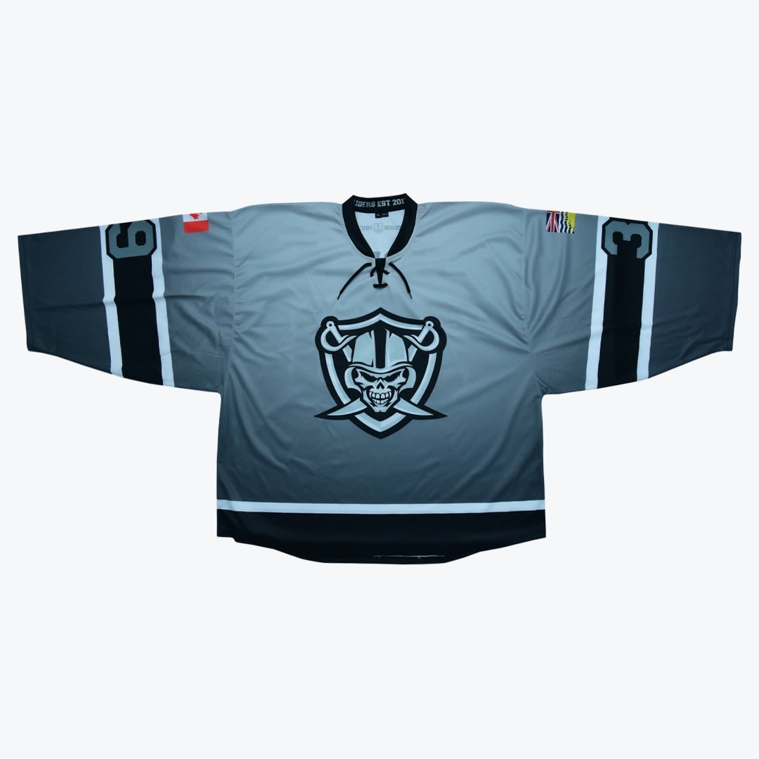 Grey and Black Raiders Hockey Jersey A grey and black gradient hockey jersey with a skull raider logo on the chest, a Canadian flag on the right shoulder, and a British Columbia flag on the left shoulder.
