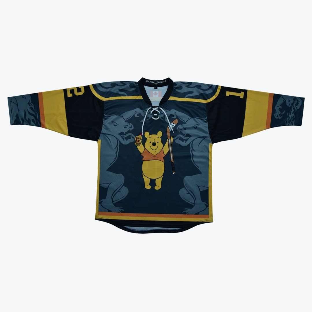 Custom Winnie the Pooh Hockey Jersey A custom hockey jersey laid flat on a white background, featuring Winnie the Pooh holding a hockey stick and a syrup bottle, flanked by two stone gargoyles on a dark blue and gold design.