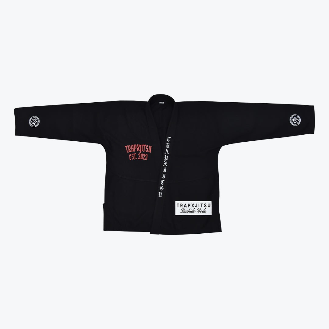 TrapXJitsu Black Gi Jacket A black BJJ gi jacket with red and white gothic-style branding, including TRAPXJITSU EST. 2023 on the chest and a Bushido Code patch on the lower left.