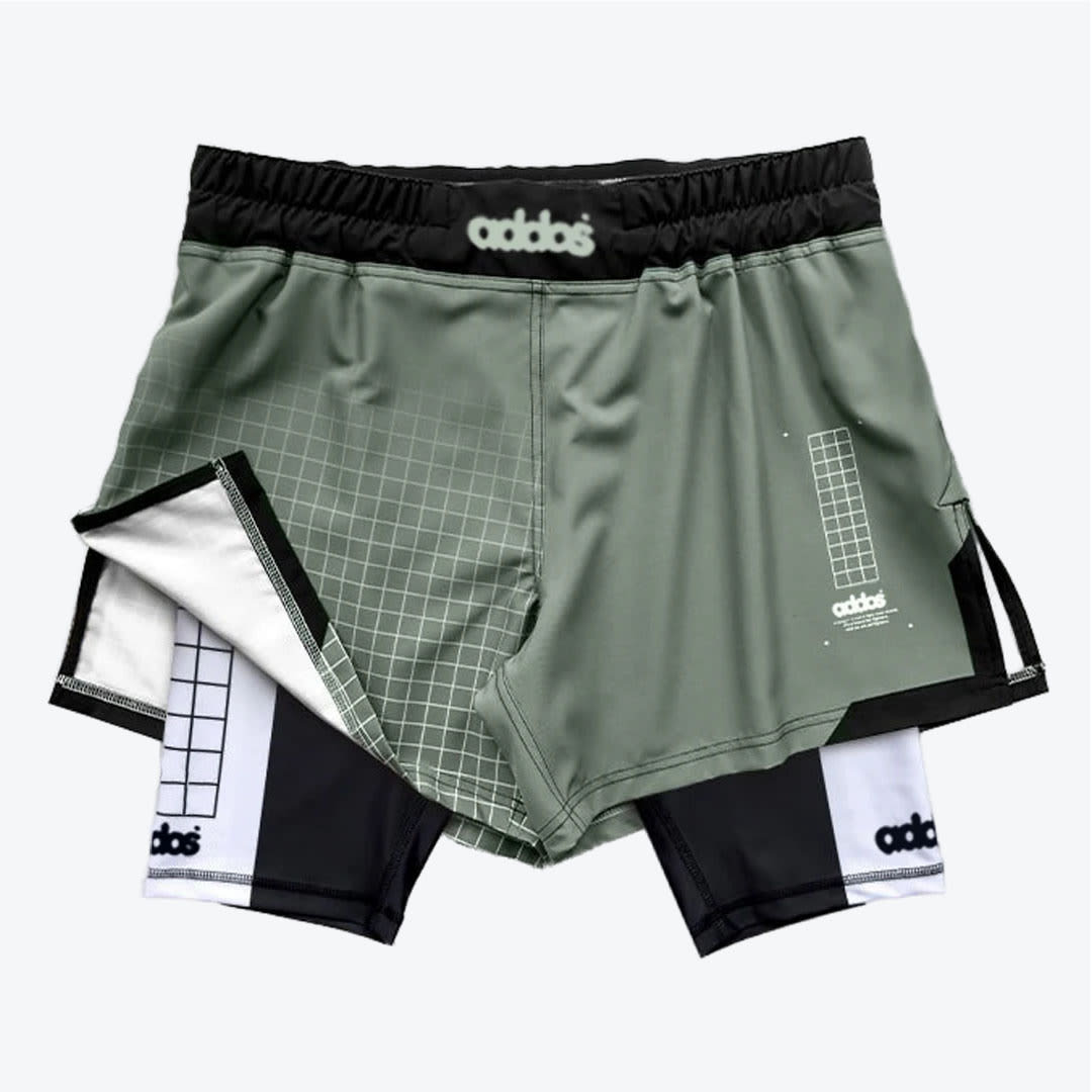 Two-in-One Athletic Shorts in Sage Green and Black A pair of sage green two-in-one athletic shorts with a black and white inner compression layer, featuring grid patterns and stylized branding.