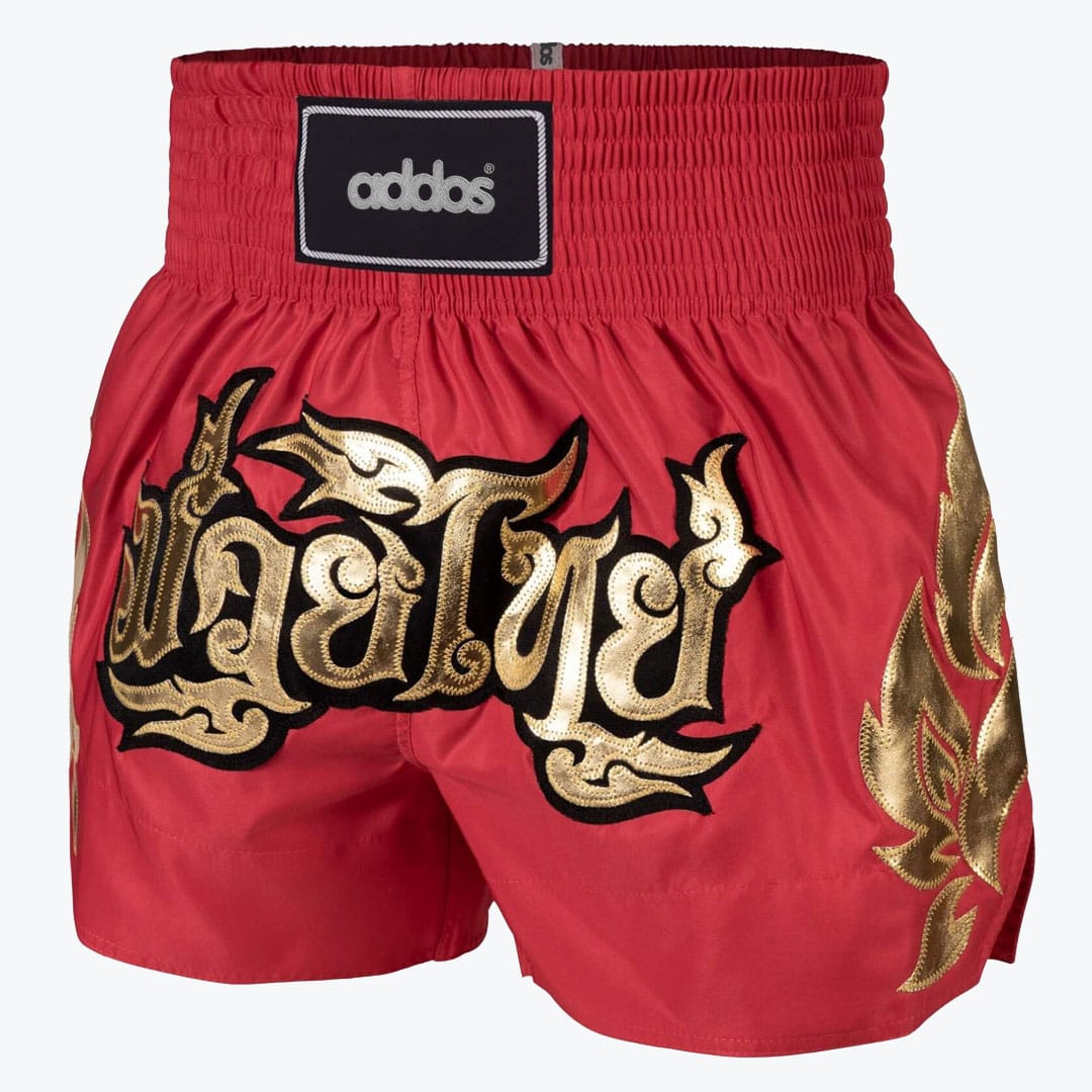 Addos Red Muay Thai Shorts Red Addos Muay Thai shorts with gold Thai lettering and flame designs on a white background.