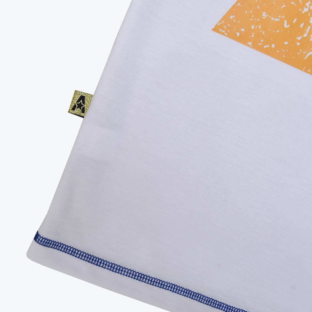Close-up of a white t-shirt hem featuring blue contrast stitching, a small gold side tag with a star logo, and a portion of an orange graphic print.