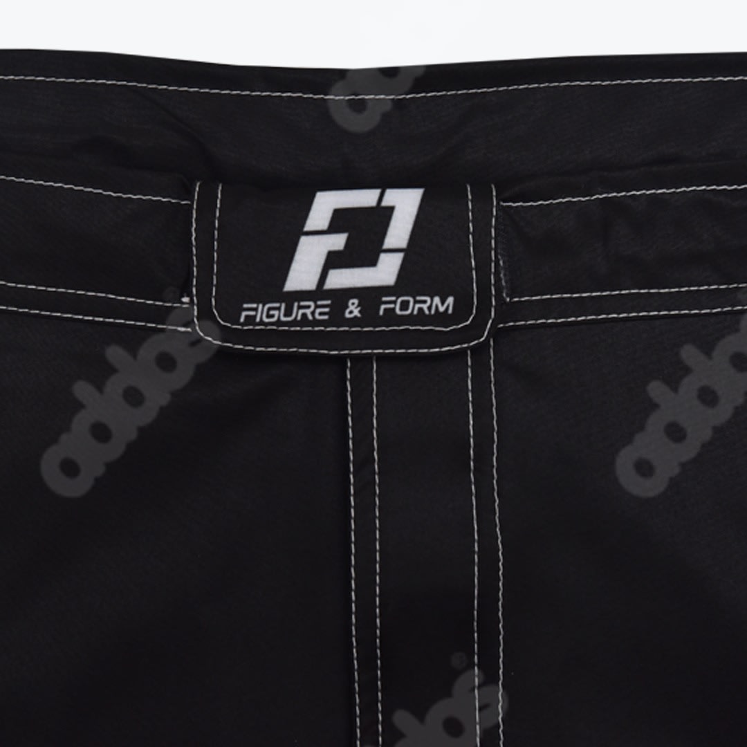 A close up shot of the waistband of black athletic shorts featuring white contrast stitching and a rectangular patch with the FIGURE & FORM logo.