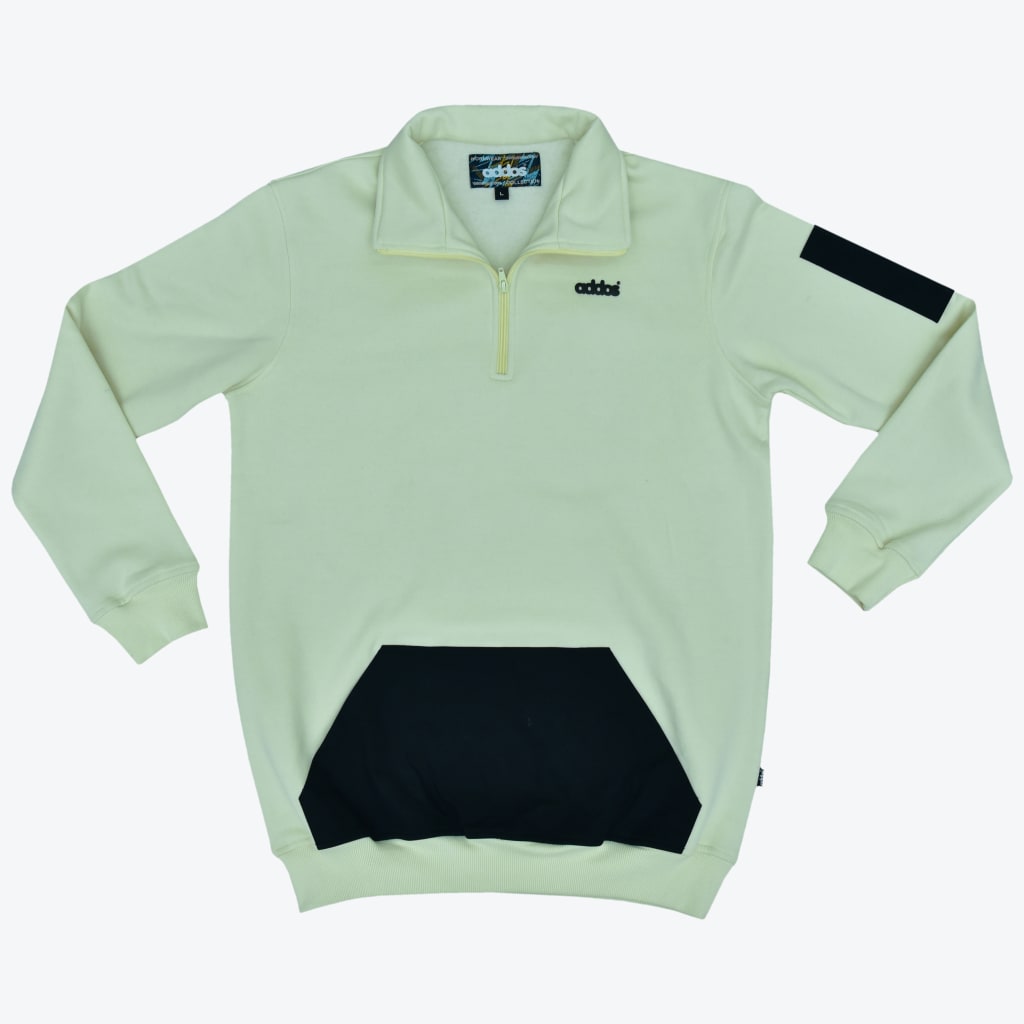 A pale yellow Addos quarter-zip sweatshirt with a black kangaroo pocket and a black patch on the left sleeve, displayed flat against a white background.
