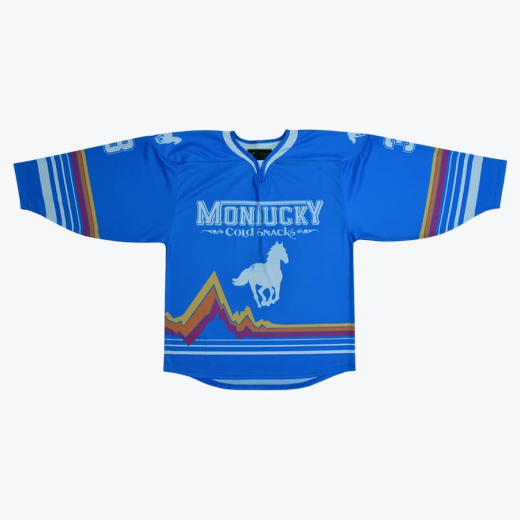 A blue hockey jersey with Montucky Cold Snacks written on the chest, a white horse graphic, and retro mountain-shaped stripes at the bottom.