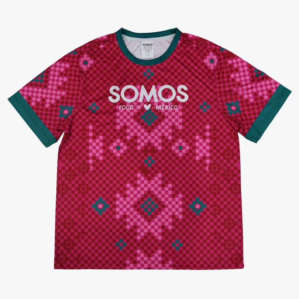 A red and pink checkered jersey t-shirt with teal collar and cuffs, featuring the white text SOMOS FOOD FROM THE HEART OF MEXICO on the chest.