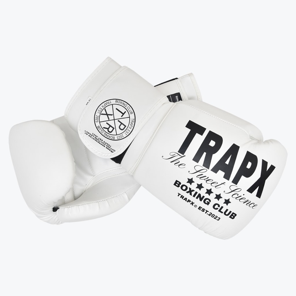 A pair of white boxing gloves with black text reading TRAPX The Sweet Science BOXING CLUB on the back of the hand and a circular logo on the wrist strap, set against a white background.