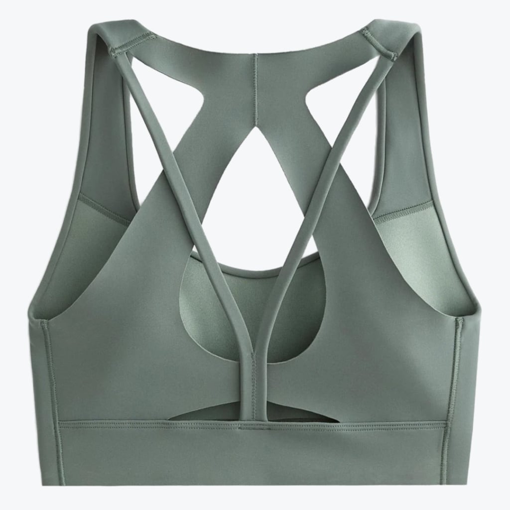 Back view of a sage green sports bra with a complex strappy design and geometric cutouts on a white background.