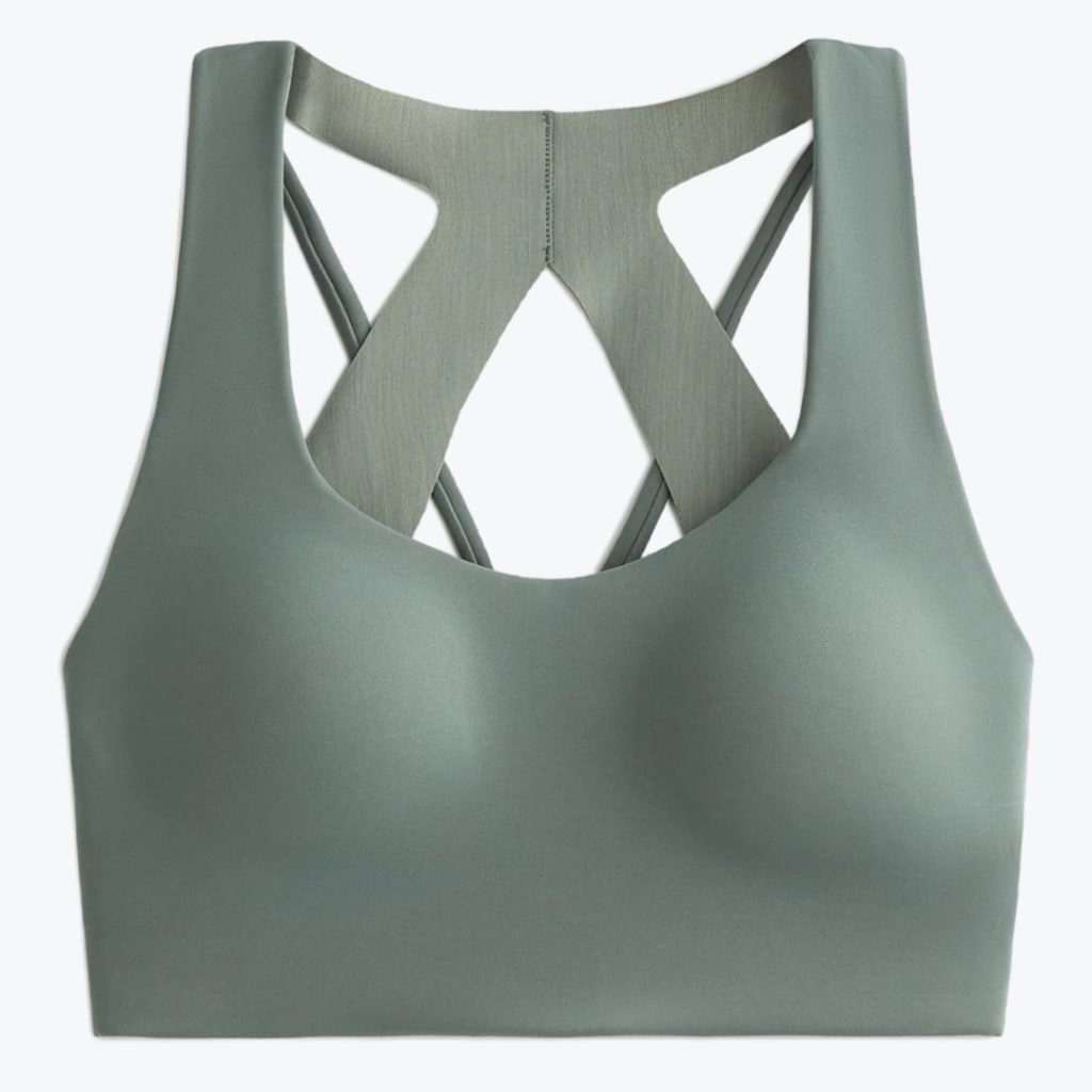 A sage green sports bra with a seamless front and a criss-cross back strap design on a white background.