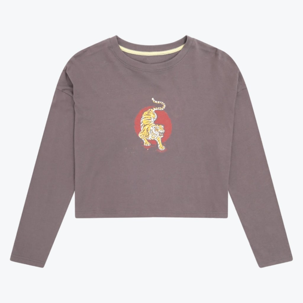 A long-sleeved cropped t-shirt in muted purple-grey with a central graphic of a yellow tiger on a red circular background, shown flat against a white backdrop.