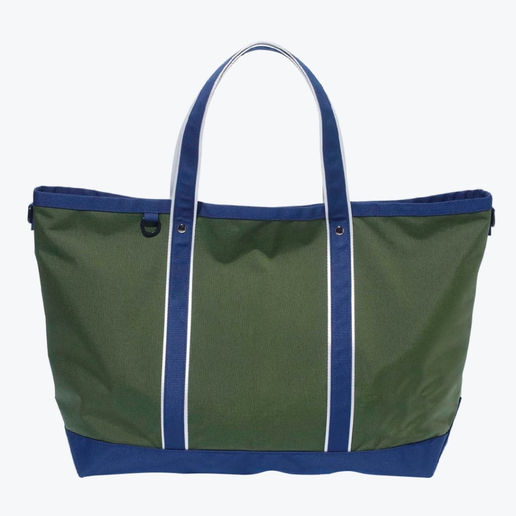 An olive green canvas tote bag with navy blue handles and base, featuring white stripes on the handles and a small D-ring on the front, isolated on a white background.
