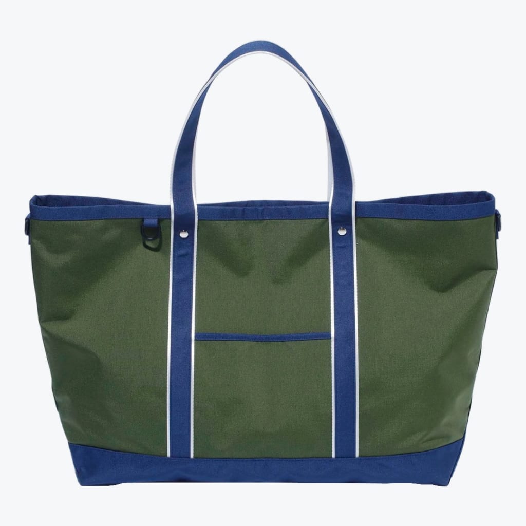 An olive green canvas tote bag with royal blue handles, bottom, and trim, featuring white stripes on the handles and a small front pocket.
