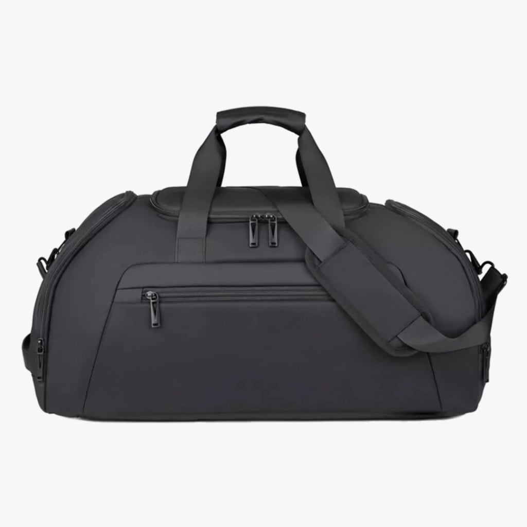 A front-facing studio shot of a matte black travel duffel bag with multiple zippered compartments, top handles, and an adjustable shoulder strap against a plain white background.