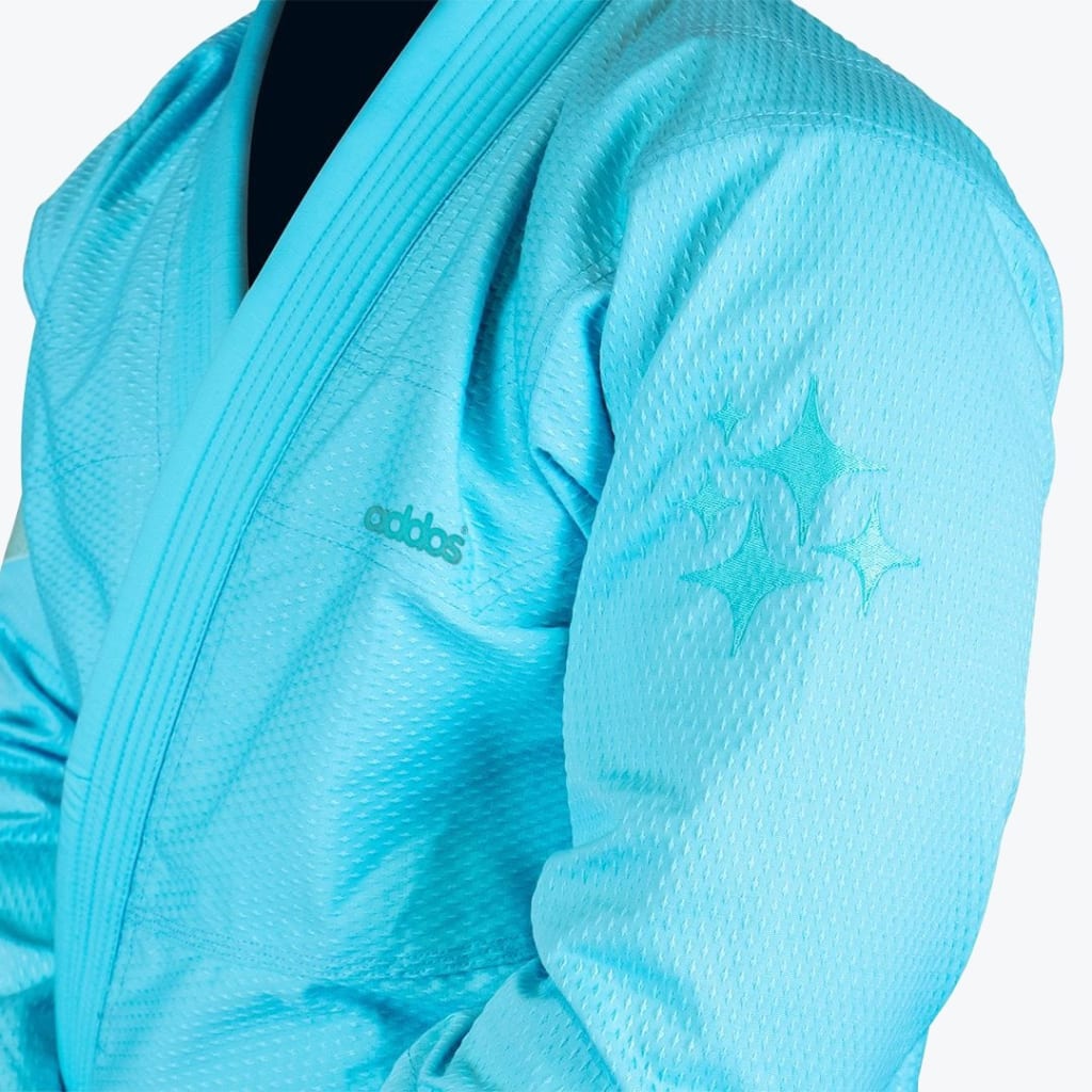 Close-up of a turquoise Addos BJJ gi jacket showing the textured fabric, chest logo, and star embroidery on the sleeve.
