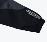 Close-up of a black and grey jacket sleeve with white text reading A BRAND REPRESENTED BY FIGHTING -CULTURE-LEGACY TRAPX EST .2023 near the elastic cuff.