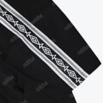 A close-up shot of black athletic fabric with faint 'adidas' logos and a prominent diagonal white stripe containing a repeating diamond pattern.