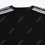 Close-up of the upper back of a black Adidas shirt, showing the crew neck, a repeating diagonal 'adidas' logo pattern on the fabric, and white and grey patterned shoulder panels.