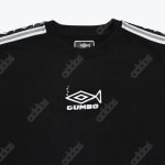 Close-up of a black sweatshirt showing a white embroidered fish logo with GUMBO text below it, set against a repeating addos patterned fabric.