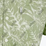 Close up of a sage green button up shirt with a white tropical leaf pattern featuring a chest pocket with a TL68 tag and white buttons