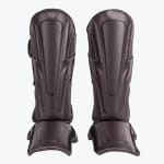 A pair of dark brown leather shin guards with instep protection, standing upright against a white background.