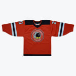 An orange hockey jersey with a cartoon bomb logo that reads TBD Bombers Hockey in the center, featuring black shoulders and striped sleeves with numbers.