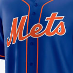 Close-up of a royal blue New York Mets baseball jersey featuring the word Mets in orange script with a white outline across the chest.